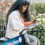 african american female with smartphone sitting on bench near bike
