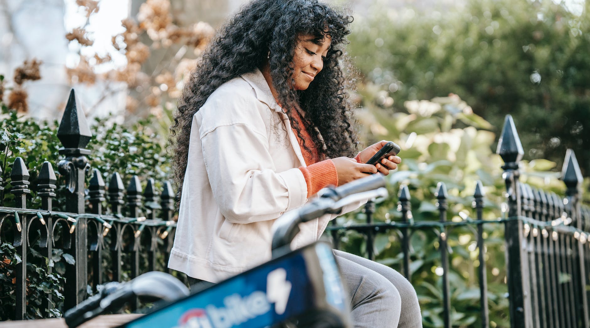african american female with smartphone sitting on bench near bike