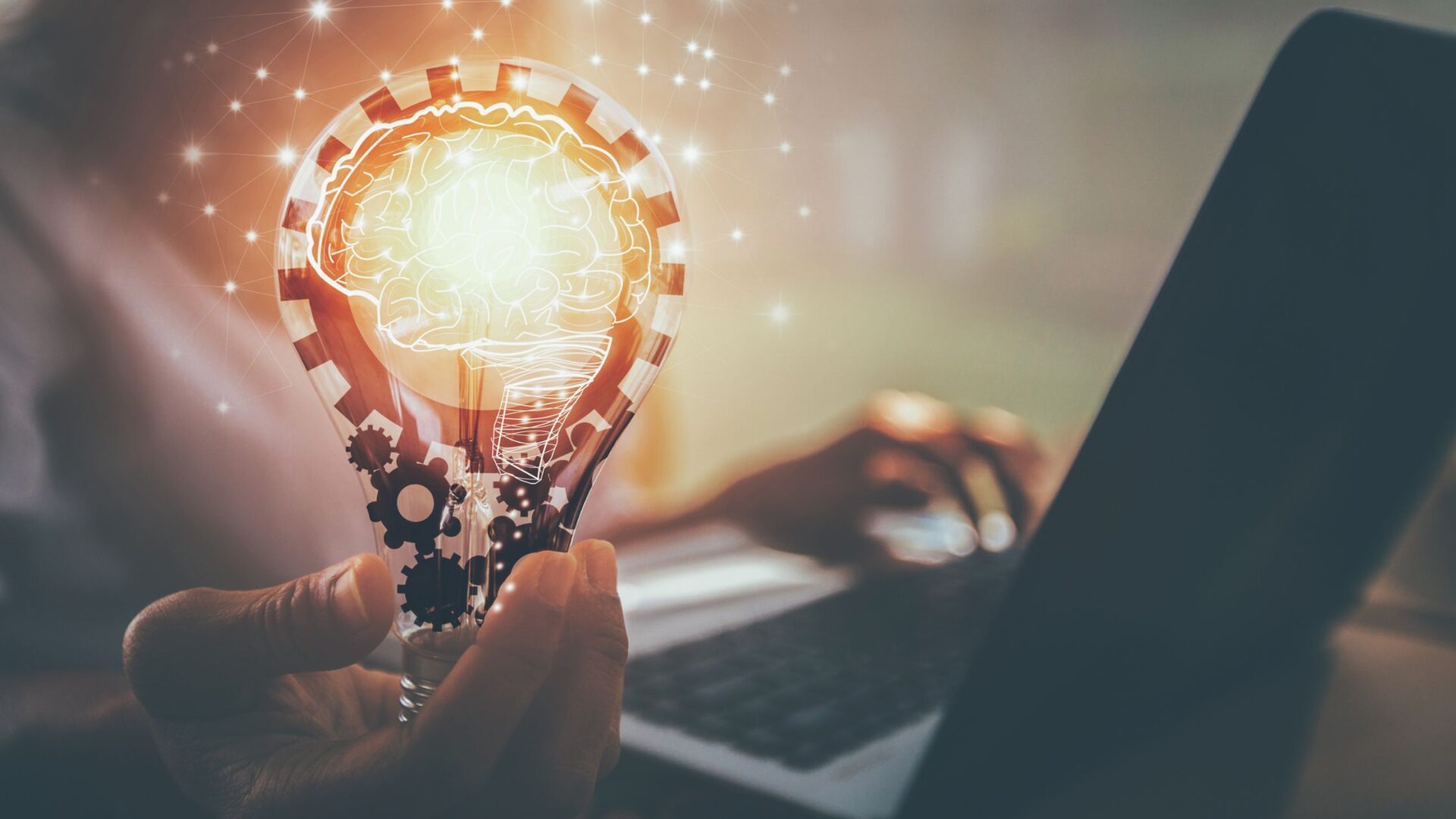 Graphic showing gears inside of a lightbulb that a person at a laptop is holding